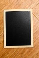 ein klein schwarz Tafel mit ein hölzern Rahmen ruht auf ein hölzern texturiert Boden. foto