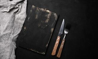 Gabel und Messer mit hölzern Griff und Schneiden Tafel auf schwarz Hintergrund foto
