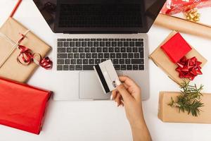 Frau, die Weihnachtsgeschenke online mit Geschenken auf Tisch kauft