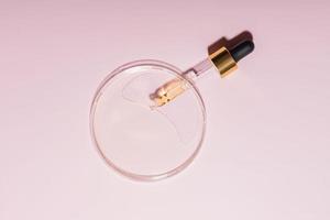 Pipette mit Stichprobe von kosmetisch Produkt im Petri Gericht auf Rosa Hintergrund, Konzept von Labor Forschung und Kosmetika testen foto