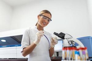 Frau Biologe mit Mikro Pipette mit Prüfung Tube und Becherglas zum Experiment im Wissenschaft Labor. Biochemie Spezialist Arbeiten mit Labor Ausrüstung und Glaswaren zum Entwicklung. foto