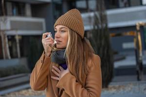 Seite Aussicht Porträt von ein Asthmatiker Frau mit ein Inhalator draußen im das Straße. jung Frau Stehen beim Straße, sie verstopft Asthma Angriff foto