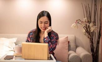 glücklich zufrieden asiatisch Frau sich ausruhen beim das Zuhause Büro Sitzung mit das Laptop nach fertig Arbeit und fühlt sich friedlich und entspannt. foto