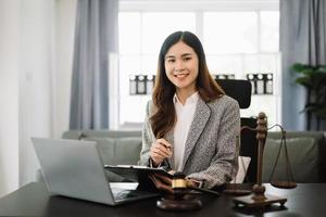 schön asiatisch Frau Anwalt Arbeiten und Hammer, Tablette, Laptop im Vorderseite, Rat Gerechtigkeit und Gesetz Konzept. im Büro foto