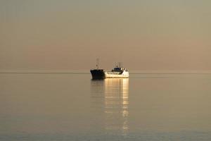 ein einsames Schiff in einem ruhigen Meer von goldener Farbe. foto