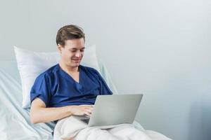 kaukasisch geduldig mit Laptop im Krankenhaus Zimmer. Mann krank geduldig Lügen im ein Krankenhaus Bett foto