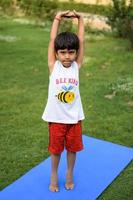 asiatisch Clever Kind tun Yoga Pose im das Gesellschaft Park draussen, Kinder- Yoga Pose. das wenig Junge tun Yoga und Meditation Übung. foto