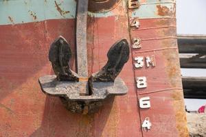 rostig Schiff Anker und Metall Oberfläche Nahansicht Sicht. rostig Schiff Körper Nahansicht mit Wasser Niveau Meter. alt und verlassen Schiff mit Anker Nahaufnahme. schwer Schiff Körper Teile auf ein Flussufer. foto