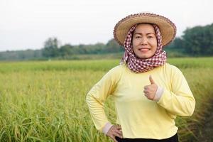 glücklich asiatisch Frau Farmer trägt Hut, Gelb Shirt, thailändisch Lendenschurz bedeckt ihr Kopf, Daumen oben , fühlt sich zuversichtlich beim Paddy Feld. Konzept, Landwirtschaft Beruf, Farmer wachsen organisch Reis. foto