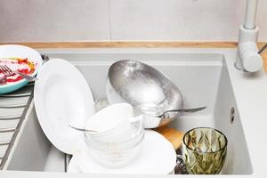 Haufen von schmutzigem Geschirr wie Teller, Besteck in der grauen modernen Granitspüle in der Küche foto