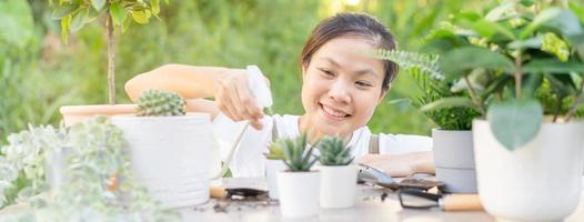 Gärtner, Sommer glücklich asiatisch Frau, sprühen, Bewässerung Pflanze Kakteen, Kaktus im Keramik Blume Topf, Wasser durch sprühen Flasche auf hölzern Tisch, nehmen Pflege im Zuhause Garten. Anlage, Gartenarbeit oder Zimmerpflanze drinnen. foto