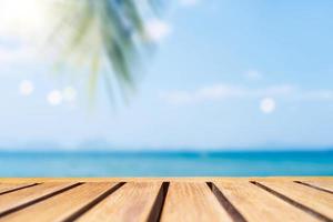 Selektiver Fokus des alten Holztischs mit einem verschwommenen schönen Strand mit tropischen Palmen, um Ihr Produkt anzuzeigen.