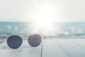 selektiver Fokus der Sonnenbrille auf dem Tisch im Sommerstrandresort mit Sonnenlichthintergrund. Urlaub Urlaub Reisetourismus. foto