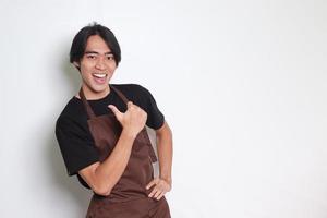 Porträt von attraktiv asiatisch Barista Mann im braun Schürze mit Daumen zeigen Weg auf leeren Raum. Werbung Konzept. isoliert Bild auf Weiß Hintergrund foto