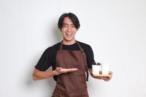 Porträt von attraktiv asiatisch Barista Mann im braun Schürze halten zwei nehmen Weg Papier Kaffee Tassen. isoliert Bild auf Weiß Hintergrund foto