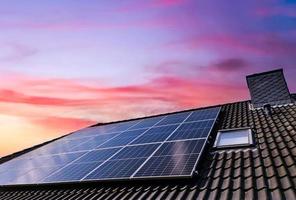 Sonnenkollektoren, die während des Sonnenuntergangs auf dem Dach eines Wohnhauses saubere Energie erzeugen. foto