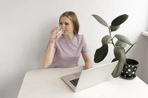 schön kaukasisch Frau Arbeiten mit Laptop während Trinken Glas von Wasser auf ein Tabelle beim heim. foto