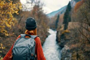 Frau Wanderer mit ein Rucksack auf ihr zurück in der Nähe von ein Berg Fluss im Natur, zurück Aussicht foto