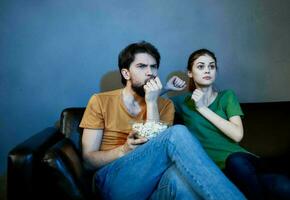 ein Frau und ein Mann mit Popcorn auf ein Leder Sofa drinnen Aufpassen Fernseher im das Abend foto