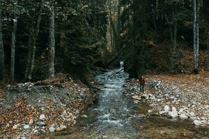 Frau Reisender in der Nähe von ein Berg Fluss im das Wald sitzt auf das Ufer Herbst Landschaft foto