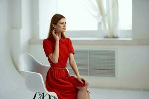 rothaarig Frau im rot Kleid Sitzung auf ein Stuhl Mode foto