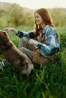 glücklich Frau Sitzung im Natur und spielen mit ihr Haustier im das Park Sitzung auf das Grün Gras im das Sommer- Sonnenlicht im das Abend, spielen im Natur foto