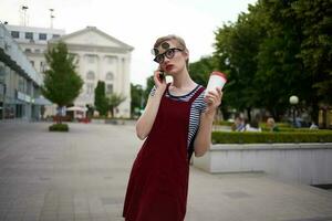 Frau mit kurz Haar auf das Straße tragen Brille Glas mit trinken gehen foto