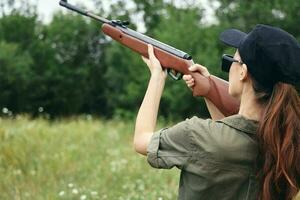 Frau auf Natur Ziel mit ein Gewehr nach oben Jagd zurück Aussicht Waffen Grün foto