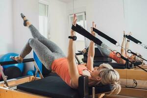 blond Frau ist ausüben auf Pilates Reformer Bett im ihr heim. foto