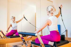 blond Frau ist ausüben auf Pilates Reformer Bett im ihr heim. foto