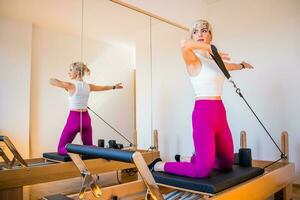 blond Frau ist ausüben auf Pilates Reformer Bett im ihr heim. foto