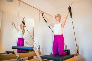 blond Frau ist ausüben auf Pilates Reformer Bett im ihr heim. foto