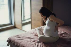 schwanger Frau mit zurück Schmerzen beim heim. Hände im das zurück. foto