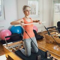 blond Frau ist ausüben auf Pilates Reformer Bett im ihr heim. foto