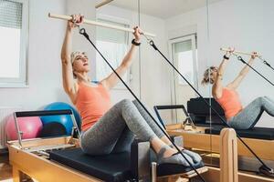 blond Frau ist ausüben auf Pilates Reformer Bett im ihr heim. foto