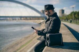 Mann ist Sitzung draussen im das Stadt und mit das Telefon. foto