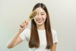 Gesundheit Haar Pflege, Lächeln schön asiatisch Frau Hand im halten Haarbürste und Bürsten, Kämmen ihr lange Gerade Haar im das Morgen Routine nach Salon Behandlung, Frisur. isoliert auf Hintergrund. foto