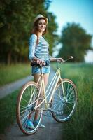 schön jung Frau im ein Hut mit ein Fahrrad im ein Park foto