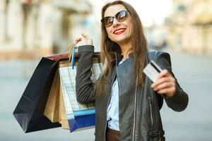 glücklich schön Frau mit Einkaufen Taschen und Anerkennung Karte im das Hände auf ein Straße foto
