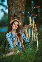 schön jung Frau im ein Hut mit ein Fahrrad im ein Park foto