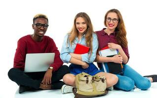 drei Studenten Sitzung mit Bücher, Laptop und Taschen isoliert auf Weiß Hintergrund foto