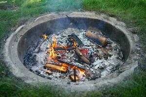 Holz Verbrennung im das Kamin. Grillen Würste Über das Lagerfeuer. Camping mit Freunde. Sommer- Feiertage. foto