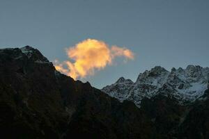 farbig Wolke Über das Nacht Berge. feurig Wolke im das Abend Über das dunkel Silhouette von Scharf Berge. Himmel beim Sonnenuntergang. Rosa hell rot Wolke im das Abend Himmel. foto