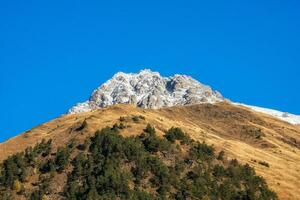 Herbst Schnee Berge beim Mittag. hell Berg Landschaft mit ein schneebedeckt Felsen im golden Sonnenlicht. natürlich Hintergrund von ein gehen durch das felsig Berge mit Scharf Felsen und Blau Himmel. foto