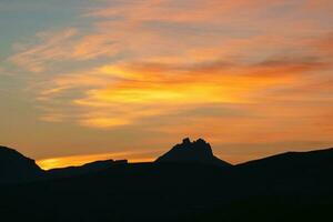 dunkel Silhouetten von Berge gegen ein hell Orange Sonnenuntergang Himmel. rot Sonnenuntergang Über majestätisch Berge. Sonnenuntergang im Magenta Töne. atmosphärisch lila Landschaft mit ein Hohe Höhe schneebedeckt Berg Schlucht. foto