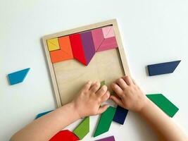 Kinder Hand sammelt mehrfarbig hölzern Mosaik auf Weiß Hintergrund. Kind löst bunt Tangram foto