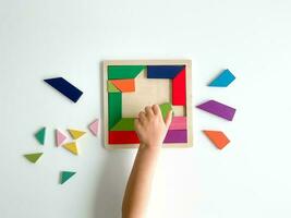 Kinder Hand sammelt mehrfarbig hölzern Mosaik auf Weiß Hintergrund. Kind löst bunt Tangram foto