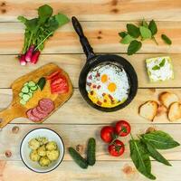 anders Essen durcheinander Eier im braten Pfanne, gekocht Kartoffeln, Quark, Croutons, Radieschen, Gurken, Tomaten, geräuchert Wurst, Croutons, Minze, Sauerampfer auf hölzern Tabelle foto