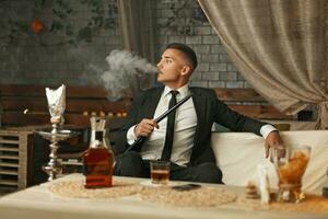 gut aussehend stilvoll Mann im ein passen Rauchen ein Huka foto
