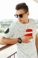 stilvoll gut aussehend Hipster Mann mit Sonnenbrille halten ein Tasse von Kaffee foto